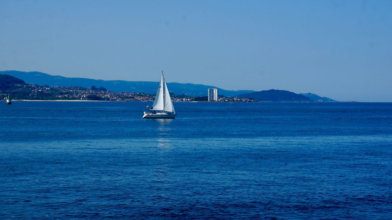 A tranquil scene of a sailboat gliding across the blue waters of Vigo Bay, Spain.