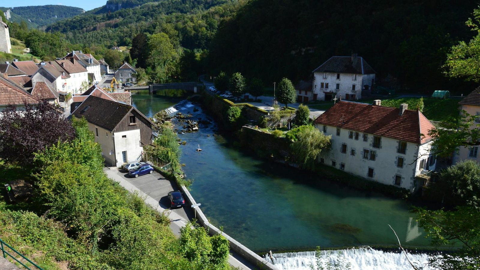 Charming river view in Lods, Bourgogne-Franche-Comté, with quaint houses and lush greenery.