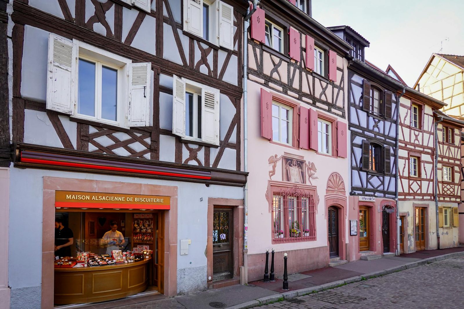 Charming street view in Alsace featuring colorful timbered houses and a local bakery.