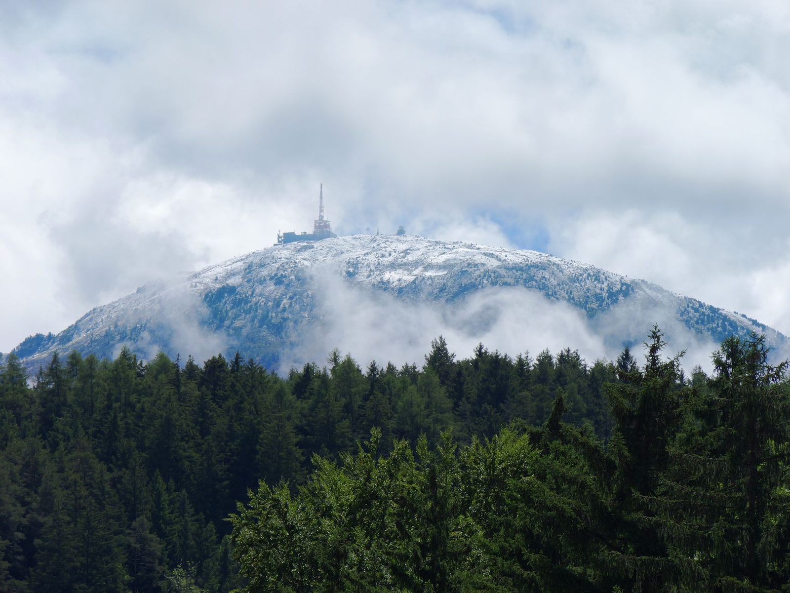 View of the snow-capped mountain summit with forest and cloudy skies in Vosges.