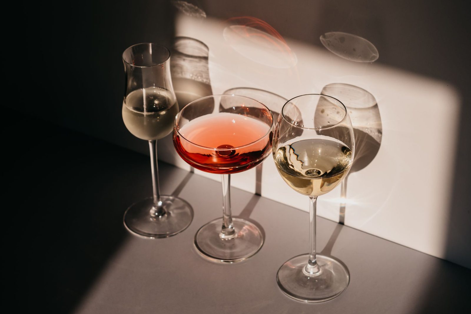 Elegant arrangement of three wine glasses casting distinct shadows in warm light.