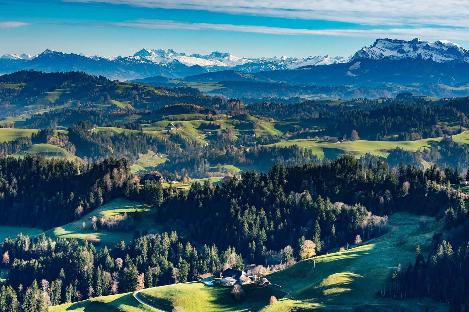 Breathtaking aerial view of Langnau im Emmental with lush hills and distant Swiss Alps under a clear sky.