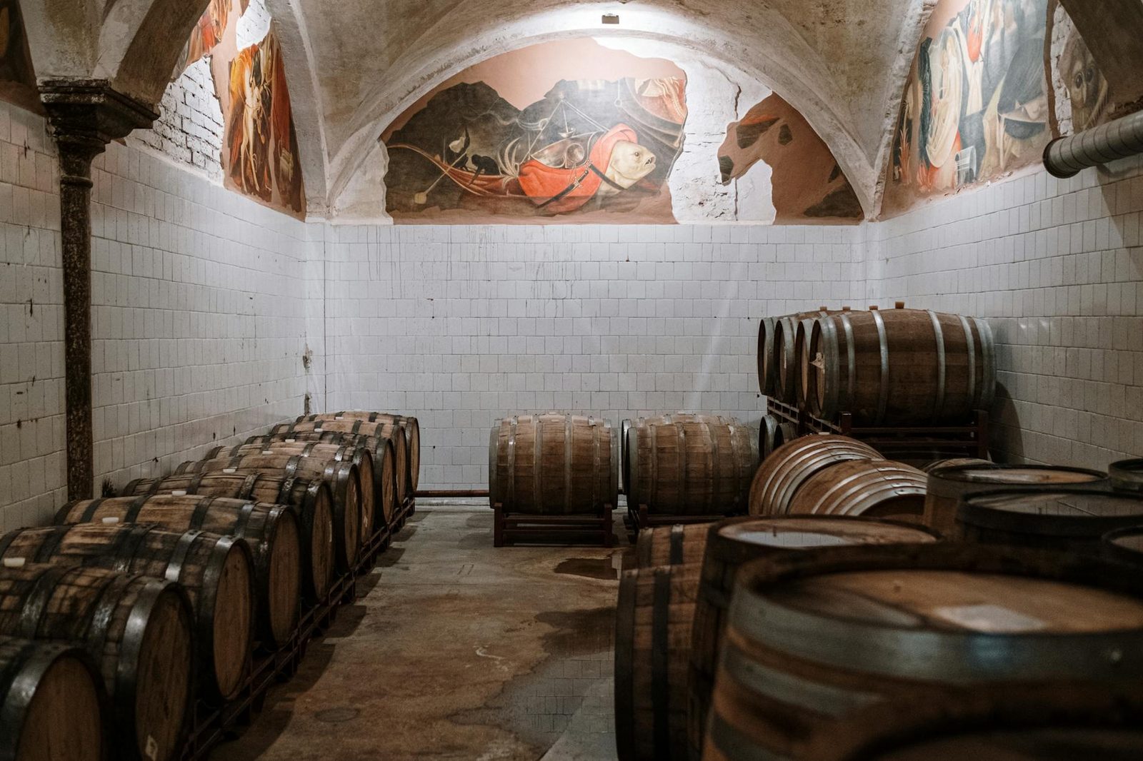 Aged wooden barrels in a historic cellar with decorative murals.