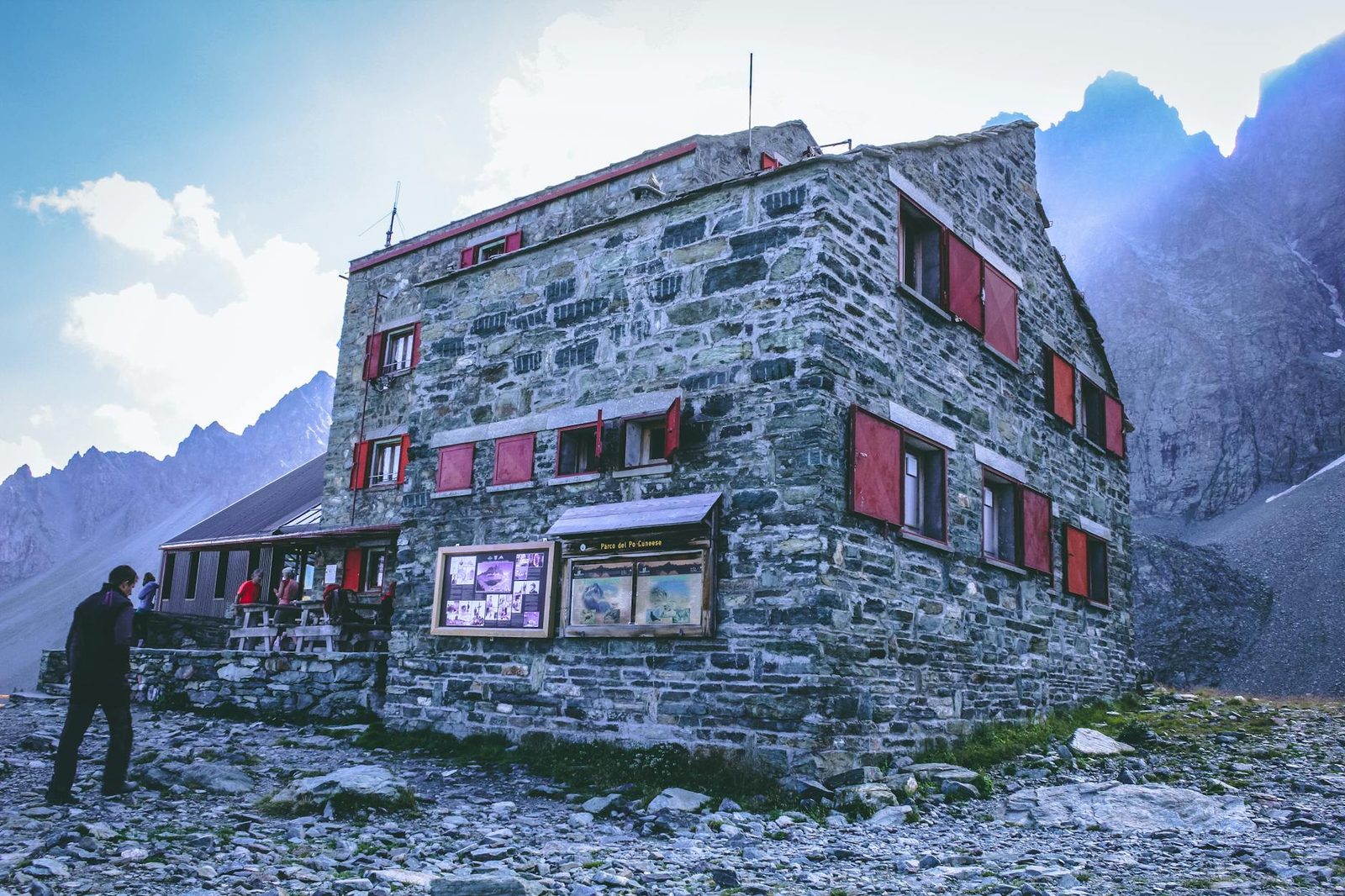 Rustic stone refuge with red shutters set in a rugged mountain landscape.