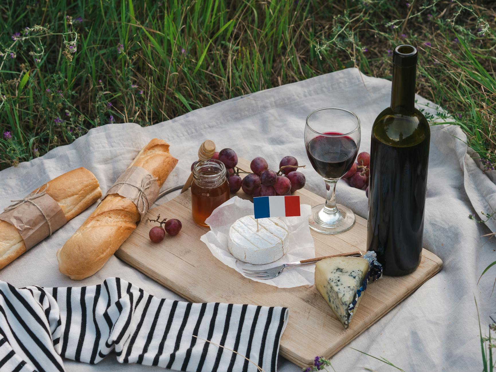Charming French picnic setup with wine, cheese, baguette, and grapes on a wooden board outdoors.