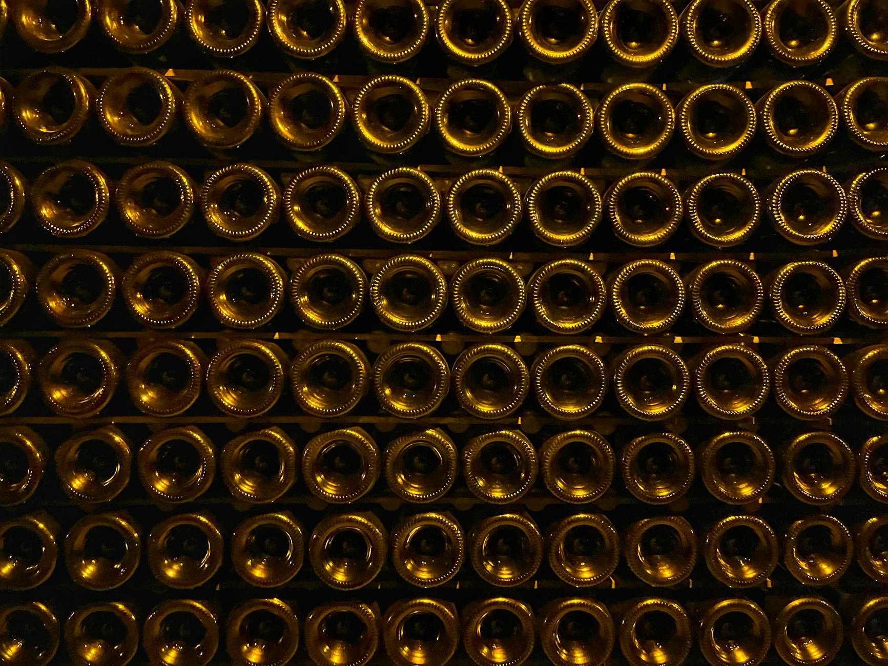 Rows of stacked wine bottles in a dimly lit cellar with elegant symmetry and warm tones.