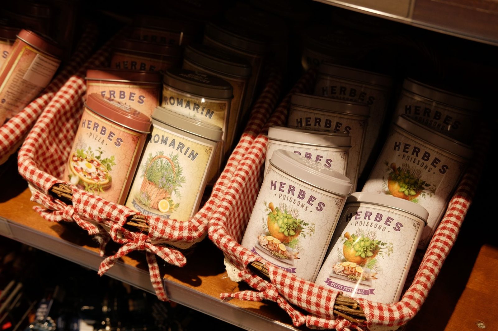 Colorful herb tins displayed in a gingham-lined basket. Perfect for kitchen décor and culinary inspiration.