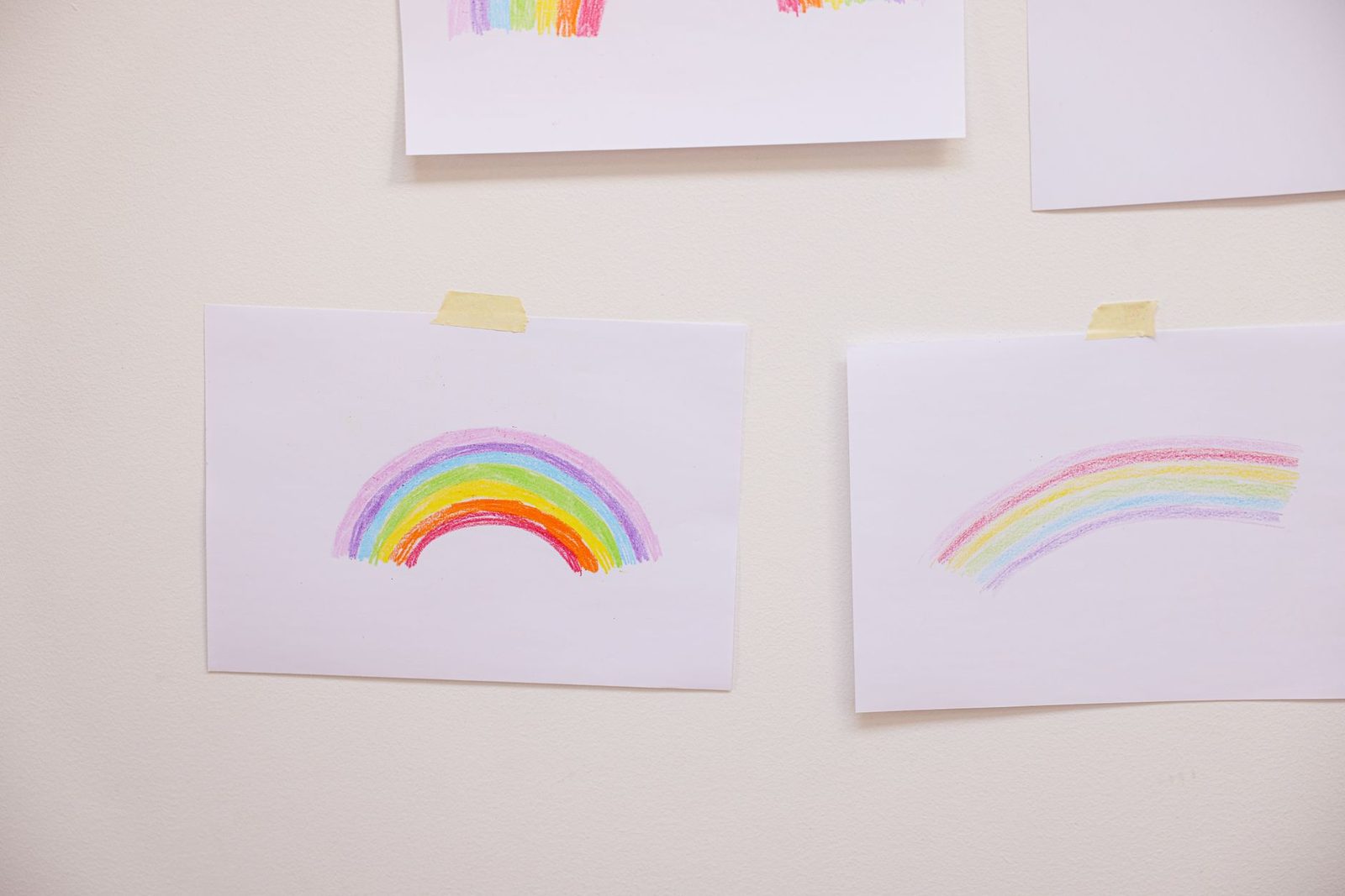Hand-drawn rainbow art on paper taped to a white wall, showcasing creativity.