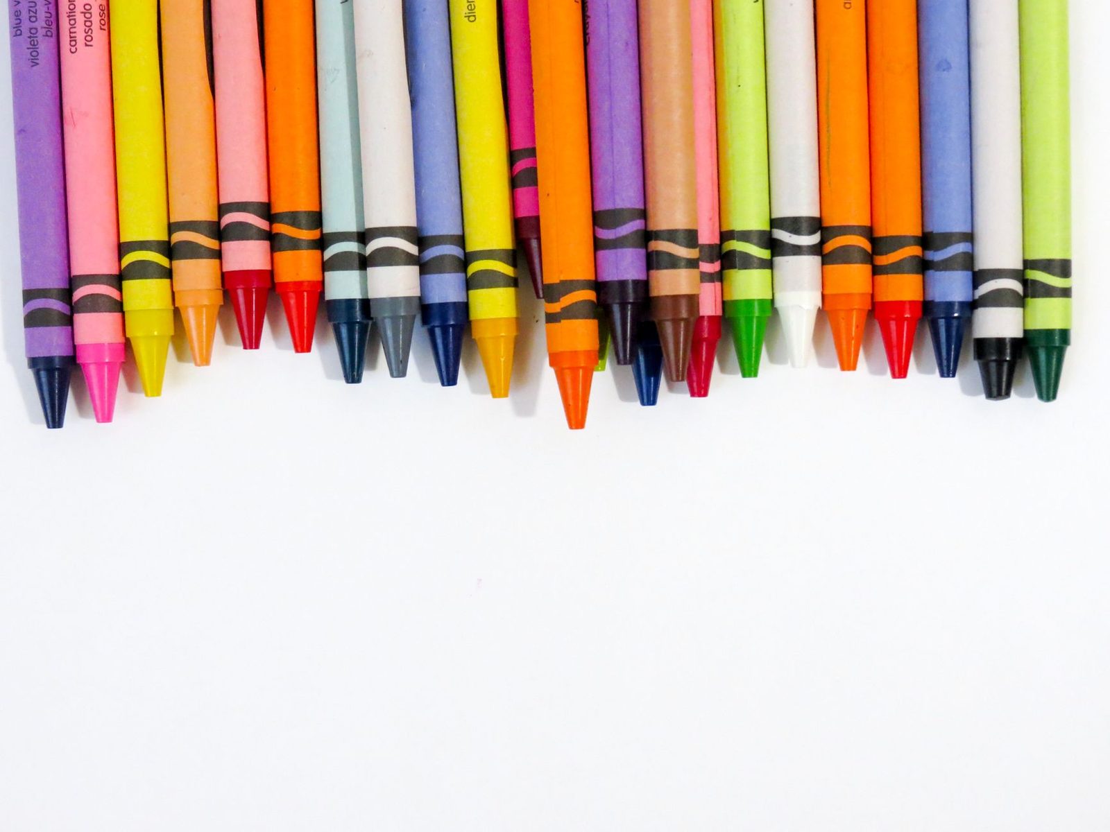 A vibrant assortment of crayons lined up on a white surface, showcasing a spectrum of colors.