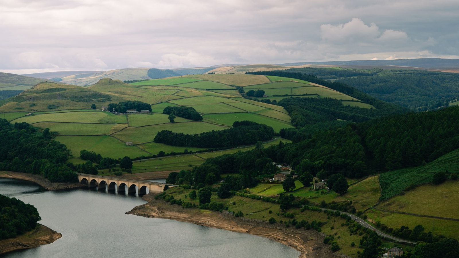 Aerial view of lush green hills and a tranquil river with an elegant stone bridge.