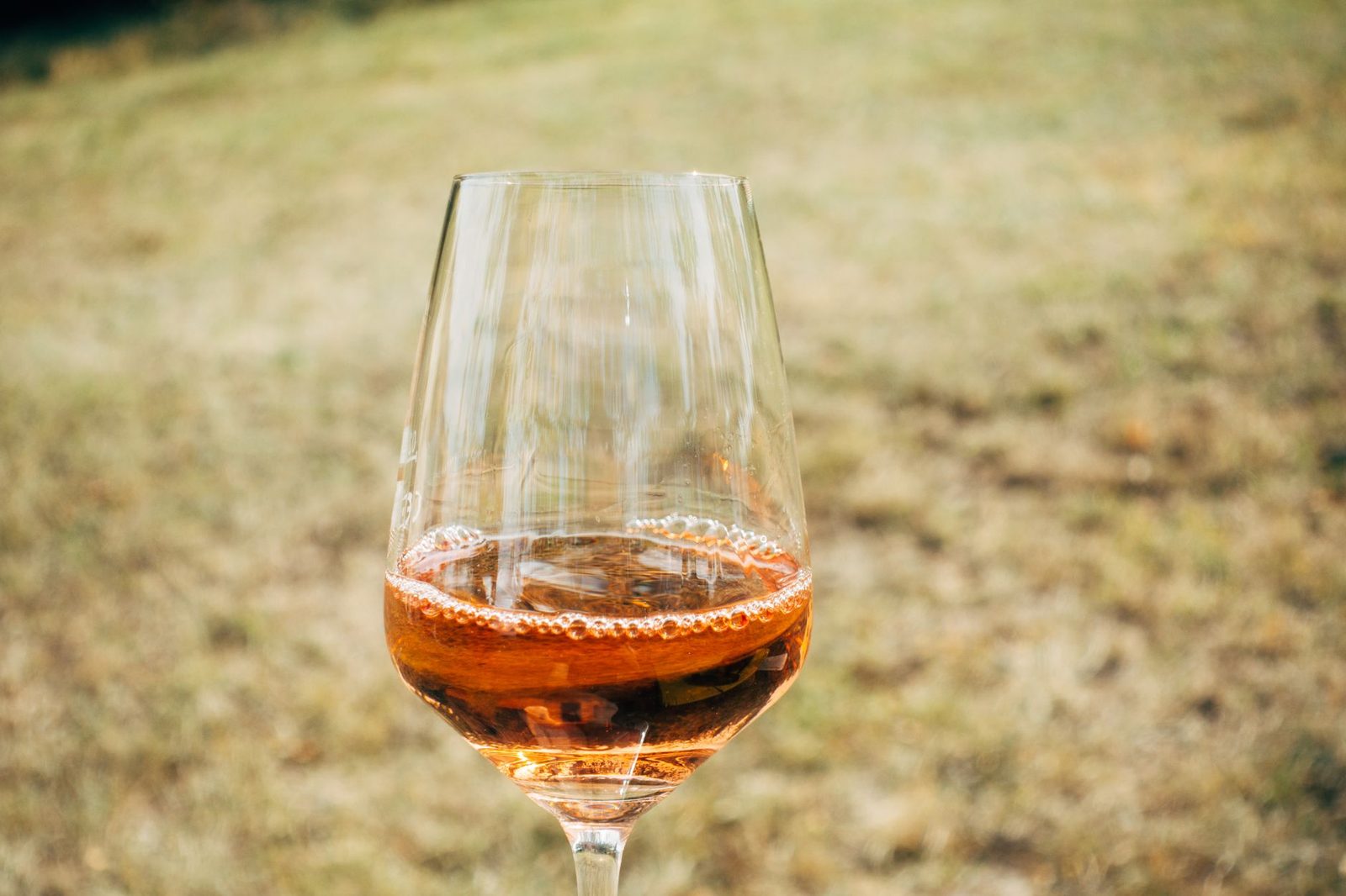 A sparkling glass of rose wine captured with a blurred outdoor background on a sunny day.