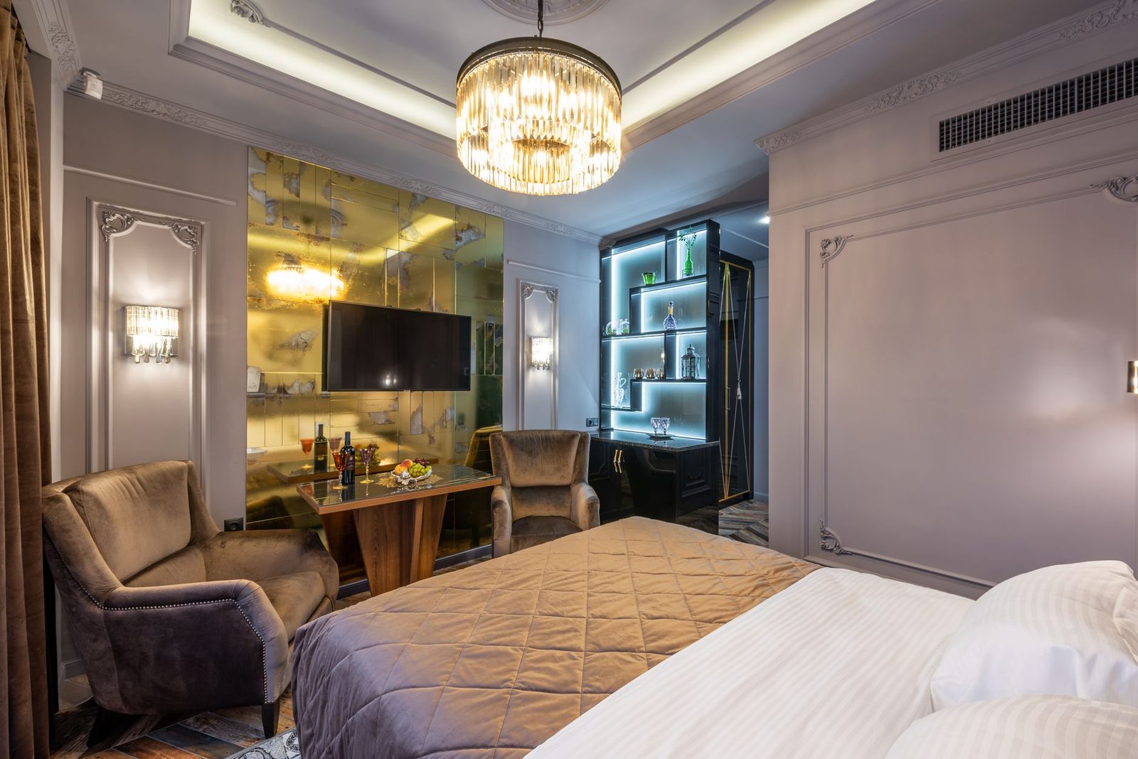 Bed with pillows and cover against armchairs in house with television set and luminous lights