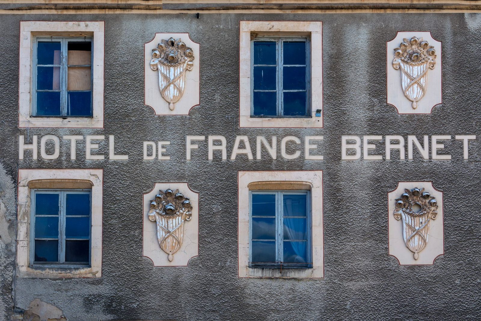 Close-up of Hotel de France Bernet facade in Saint-Saulge, showcasing vintage windows and ornate design elements.