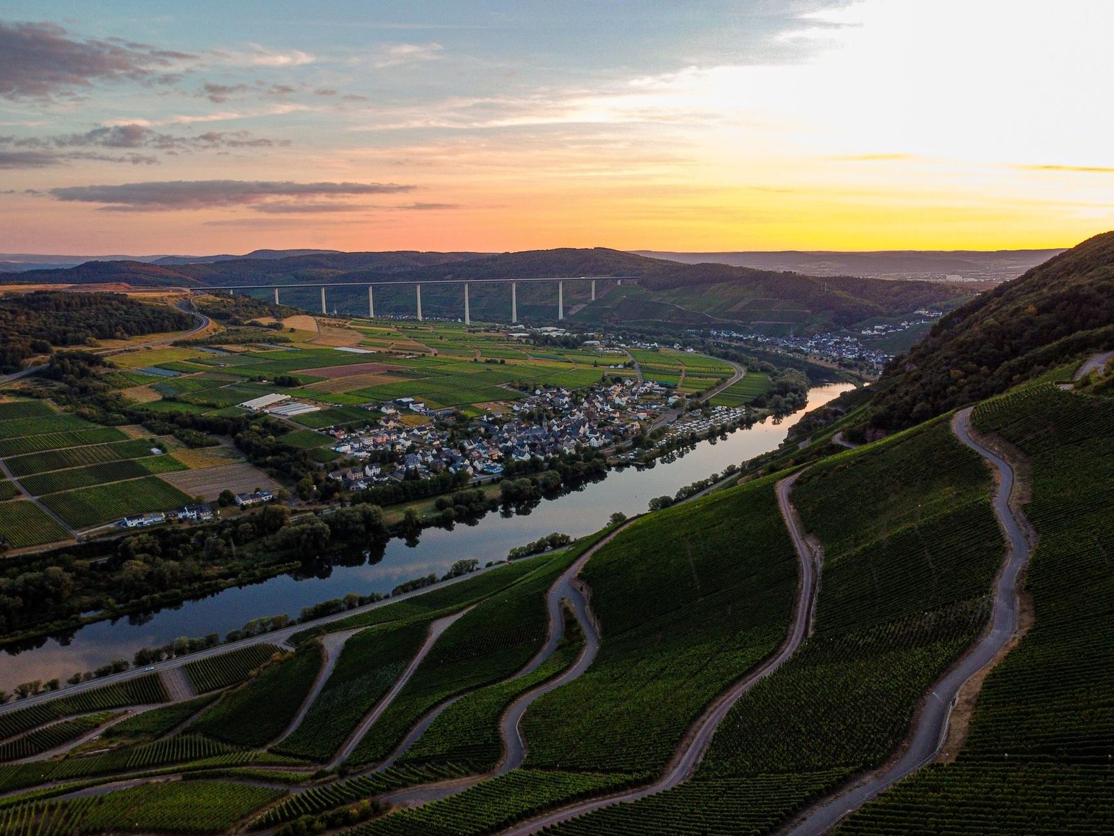 Stunning aerial view of Malroy village in Grand Est, France with vineyards and a river at sunset.