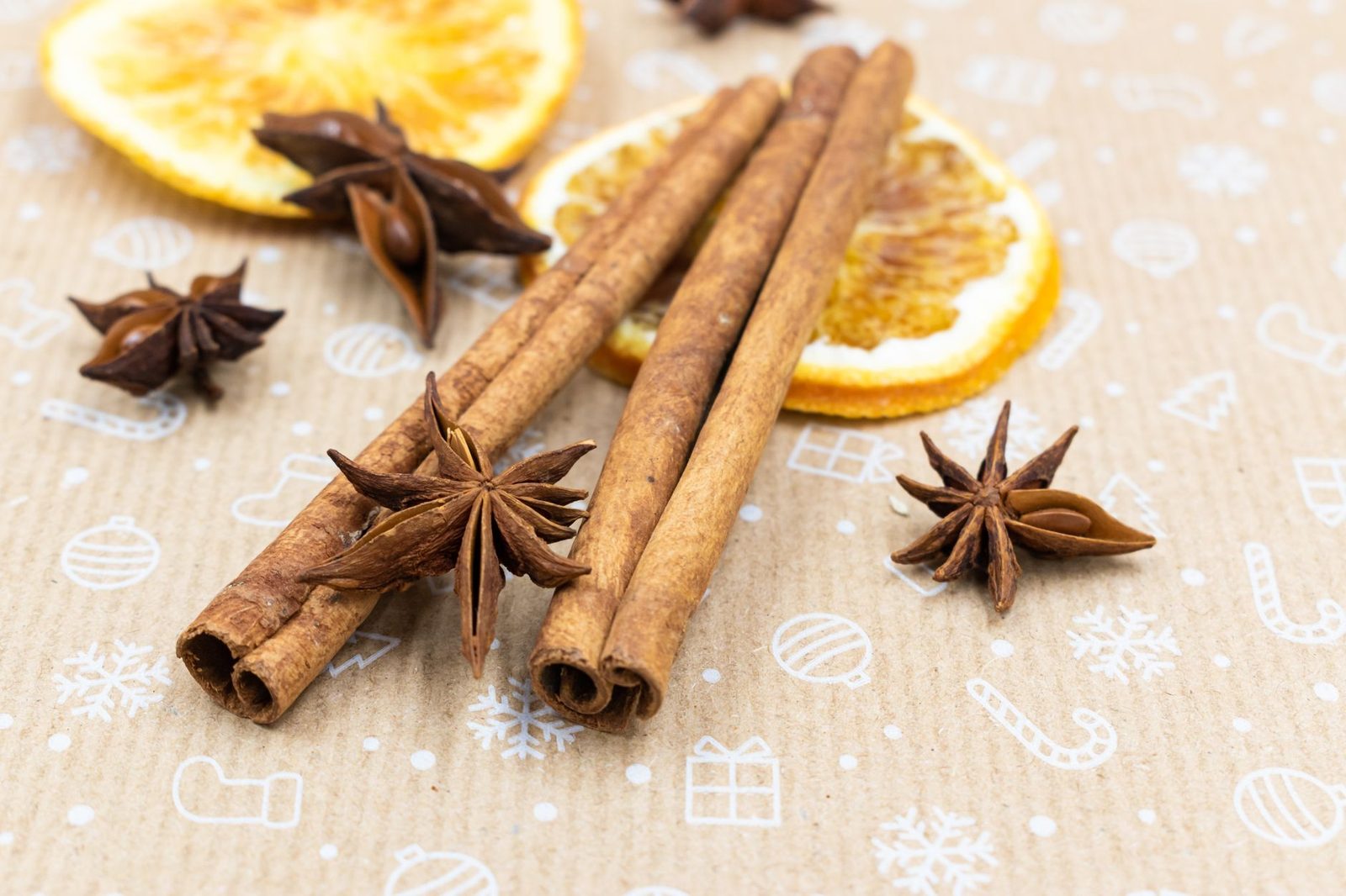 Close-up of cinnamon sticks, star anise, and dried orange slices on festive paper.