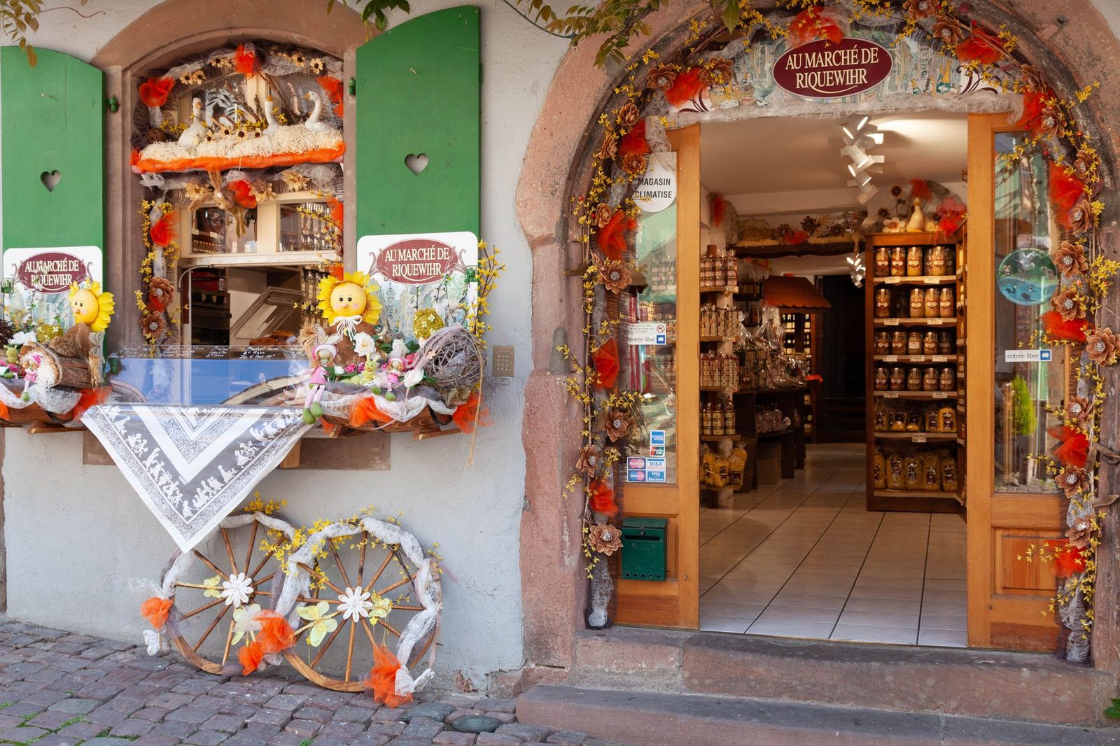 Colorful facade of a shop in Riquewihr, France, with floral decor and rustic elements.