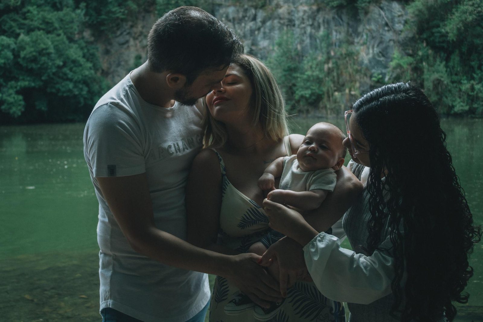 A family enjoying a tender moment together by a peaceful lake surrounded by lush greenery.