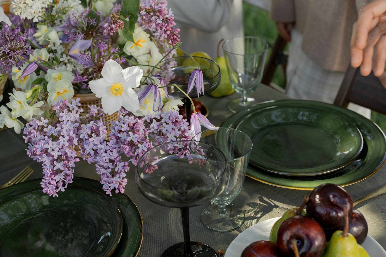 A beautifully arranged outdoor table with flowers, fruits, and green plates.