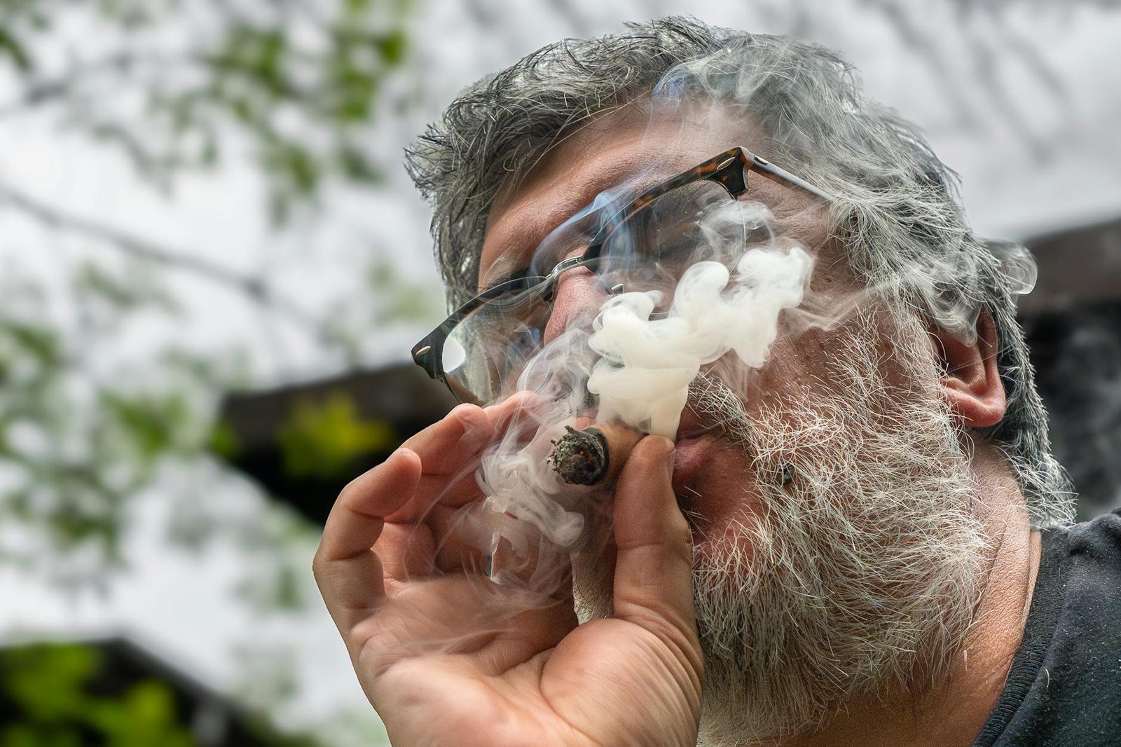 Elderly man with glasses smoking a cigar outdoors, creating a relaxed atmosphere.