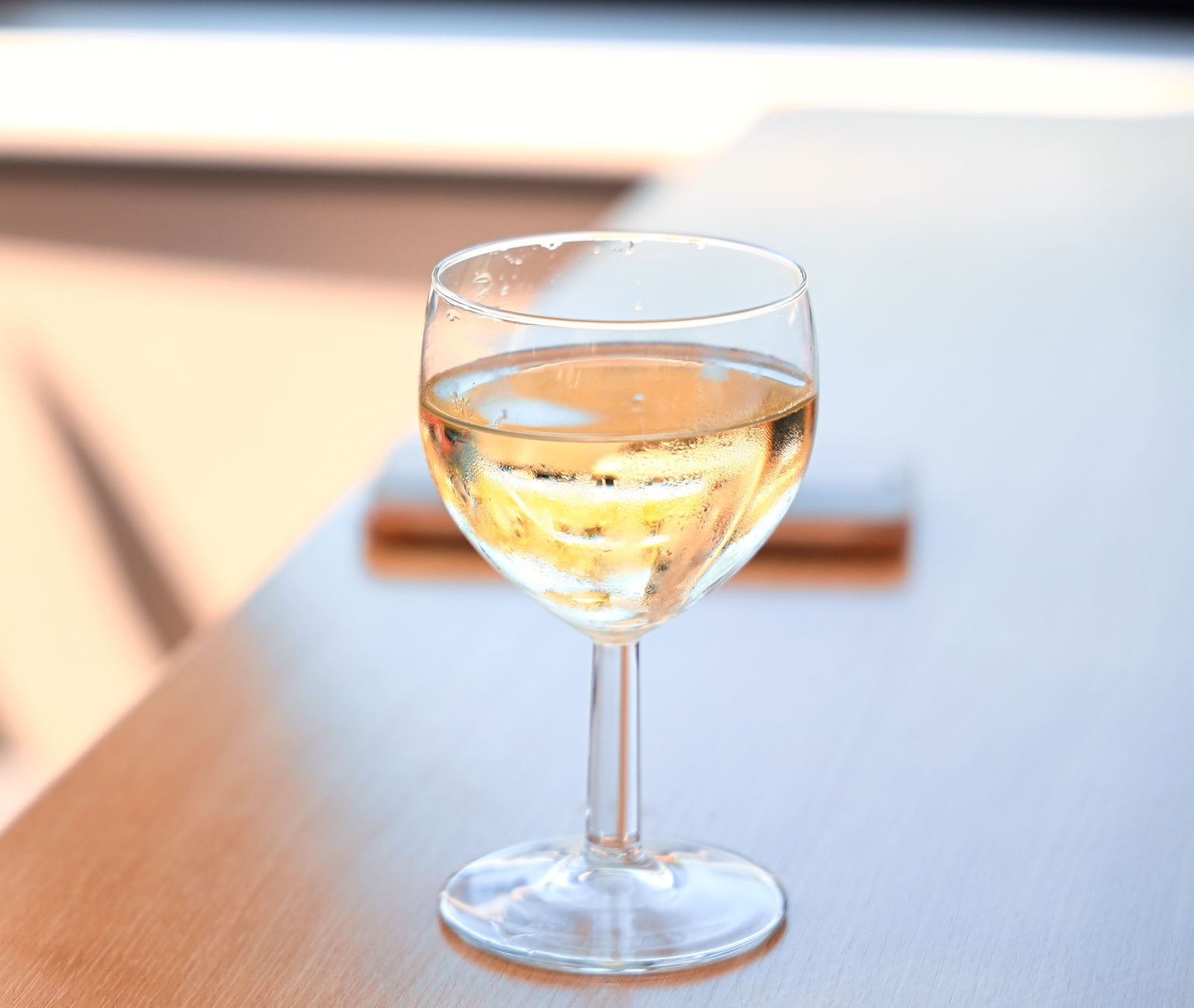A glass of chilled white wine on a wooden table with selective focus, capturing a relaxed mood.
