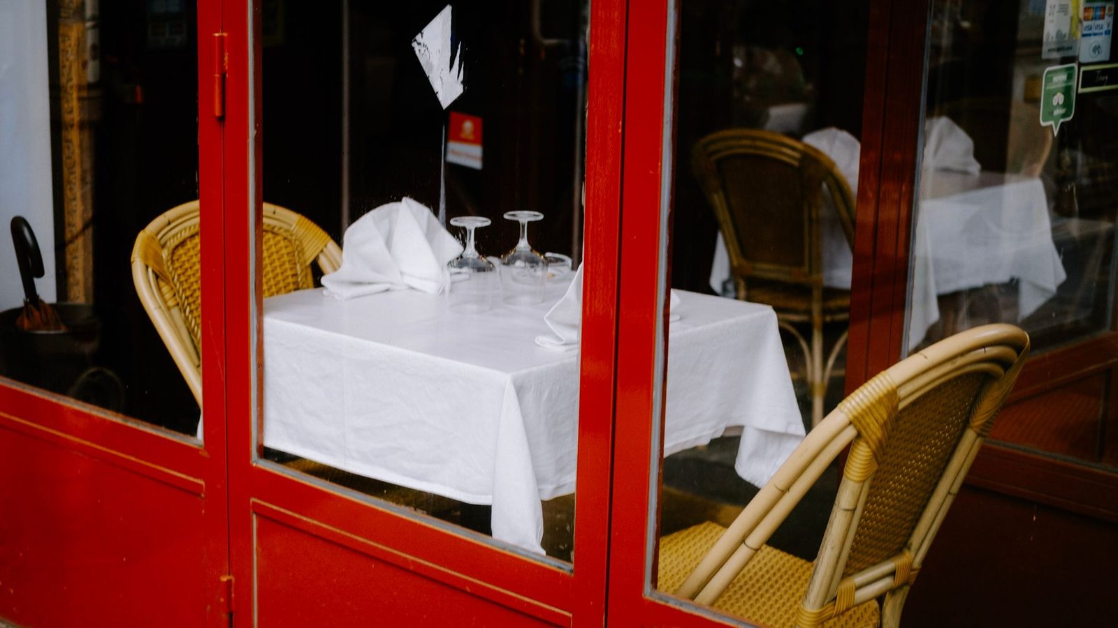 Charming restaurant table with glassware behind red door, perfect for cozy dining.