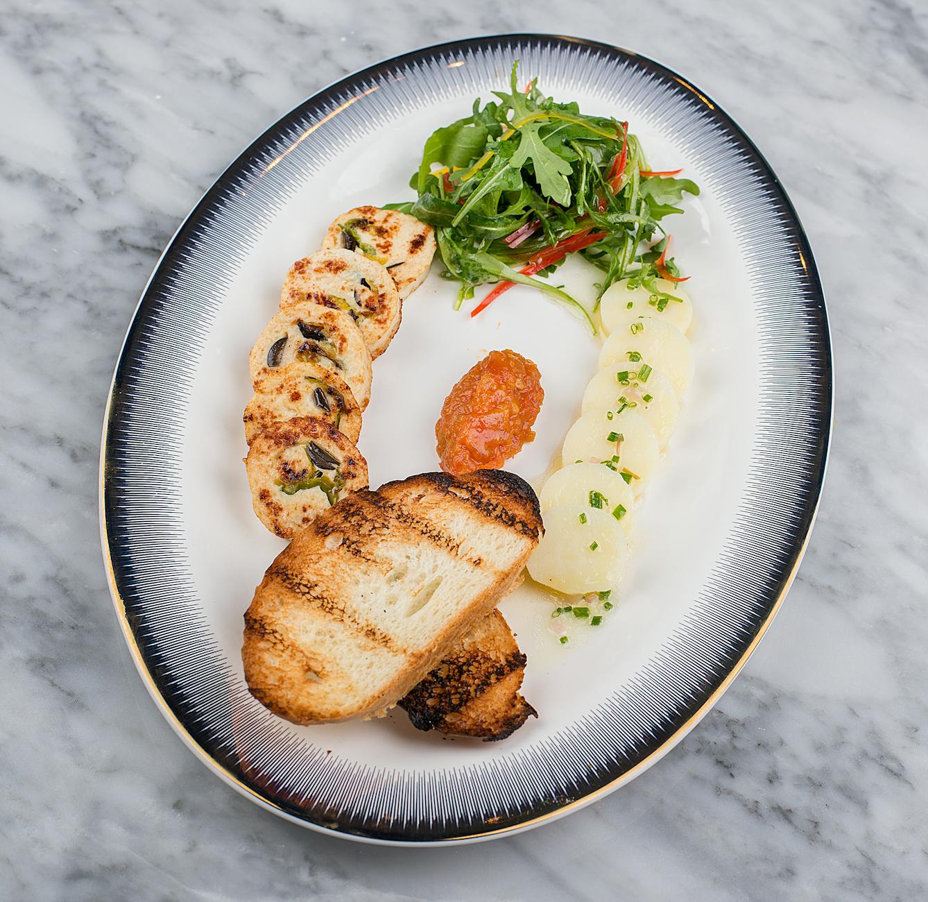 Elegant gourmet dish featuring grilled bread, salad, potatoes and chutney on a ceramic plate.