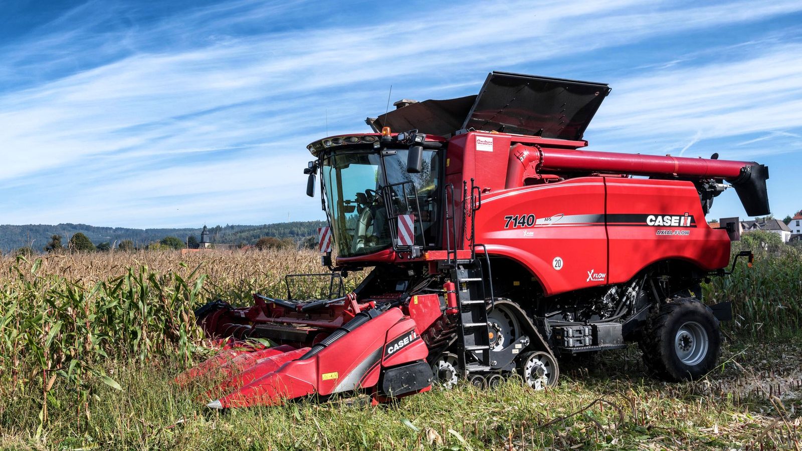 A red harvester working in a cornfield under a clear sky in rural Kassel, Germany.