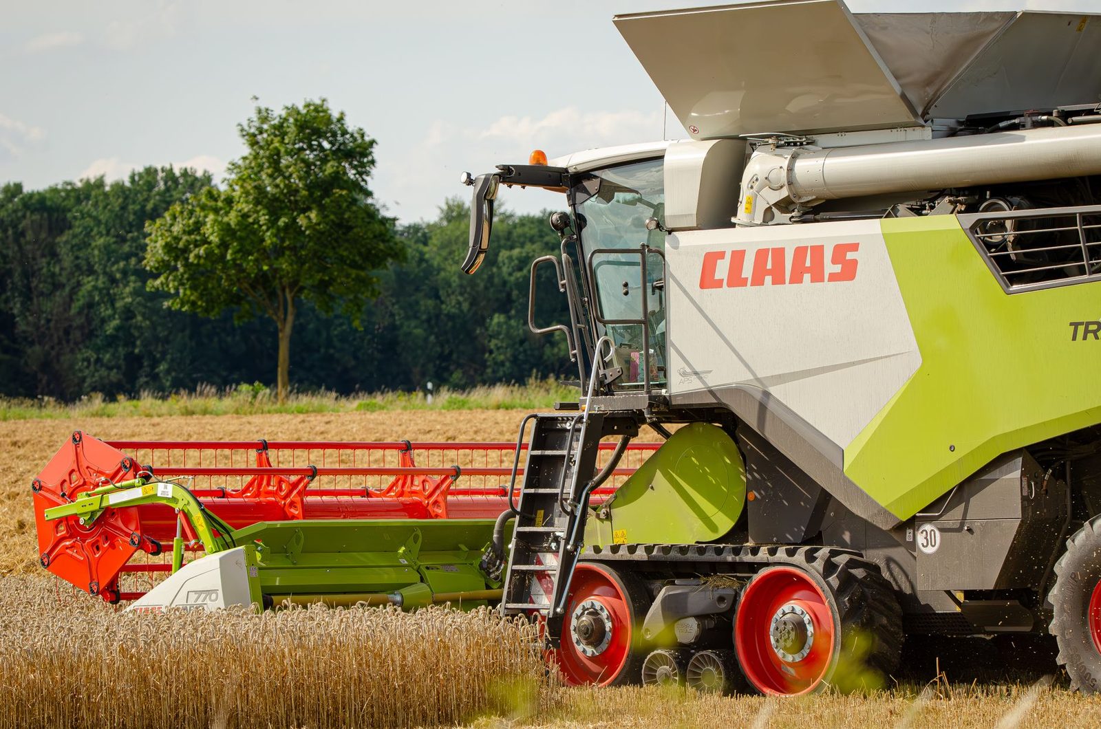 A modern CLAAS combine harvester efficiently working in a golden wheat field on a sunny summer day.