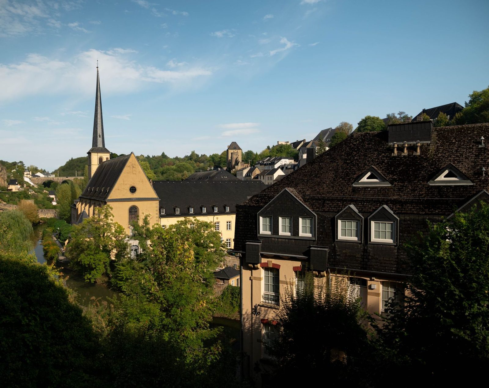 A picturesque view of Luxembourg City featuring historic architecture and lush greenery under a clear blue sky.
