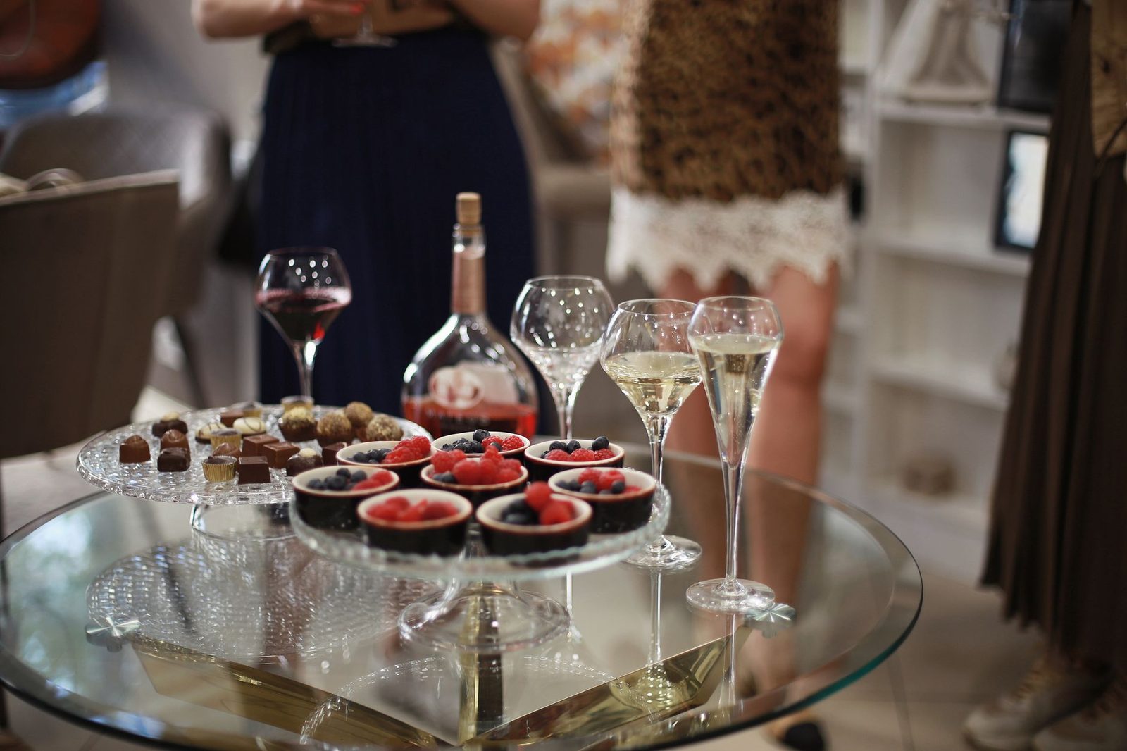 Elegant glass table setup with desserts and wine, featuring berries and chocolate treats, perfect for social gatherings.