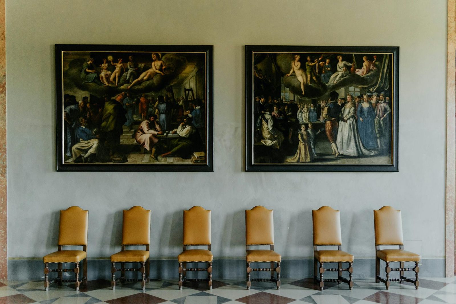 A beautifully designed interior with ornate paintings and classic wooden chairs lined up against the wall.