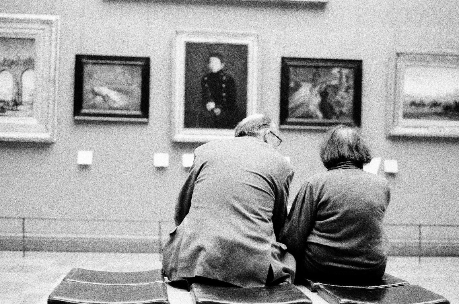 Black and white photo of an elderly couple admiring art in a museum.