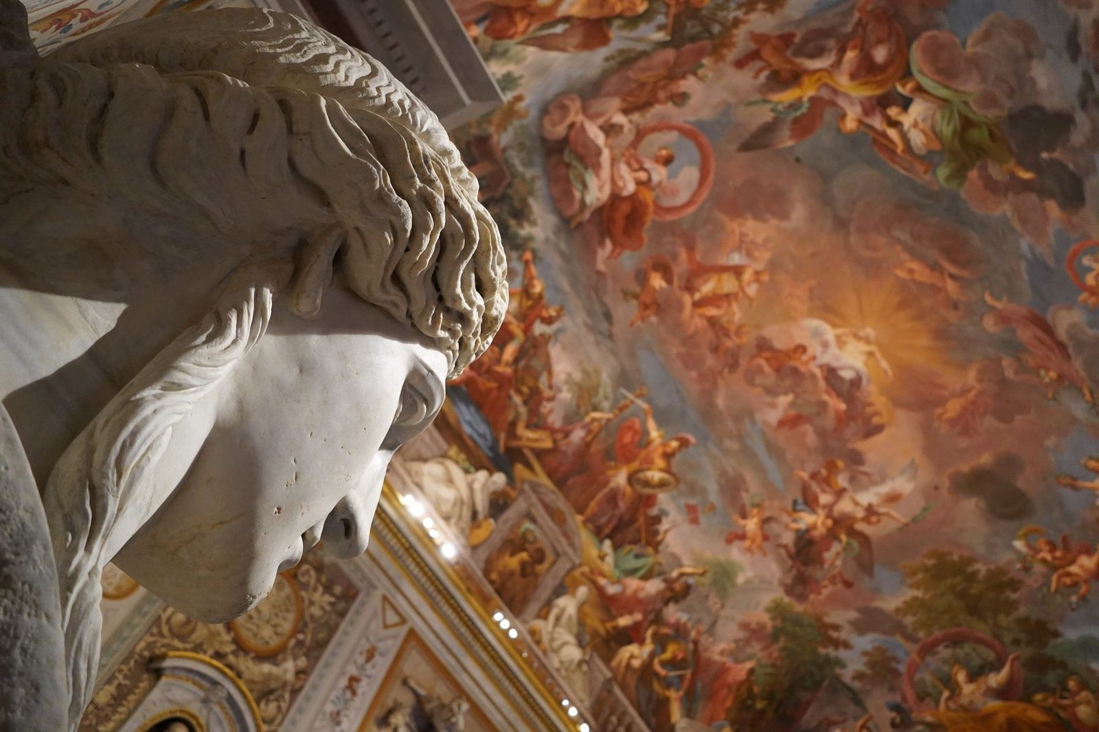 Close-up of a marble sculpture with a frescoed ceiling in a museum.
