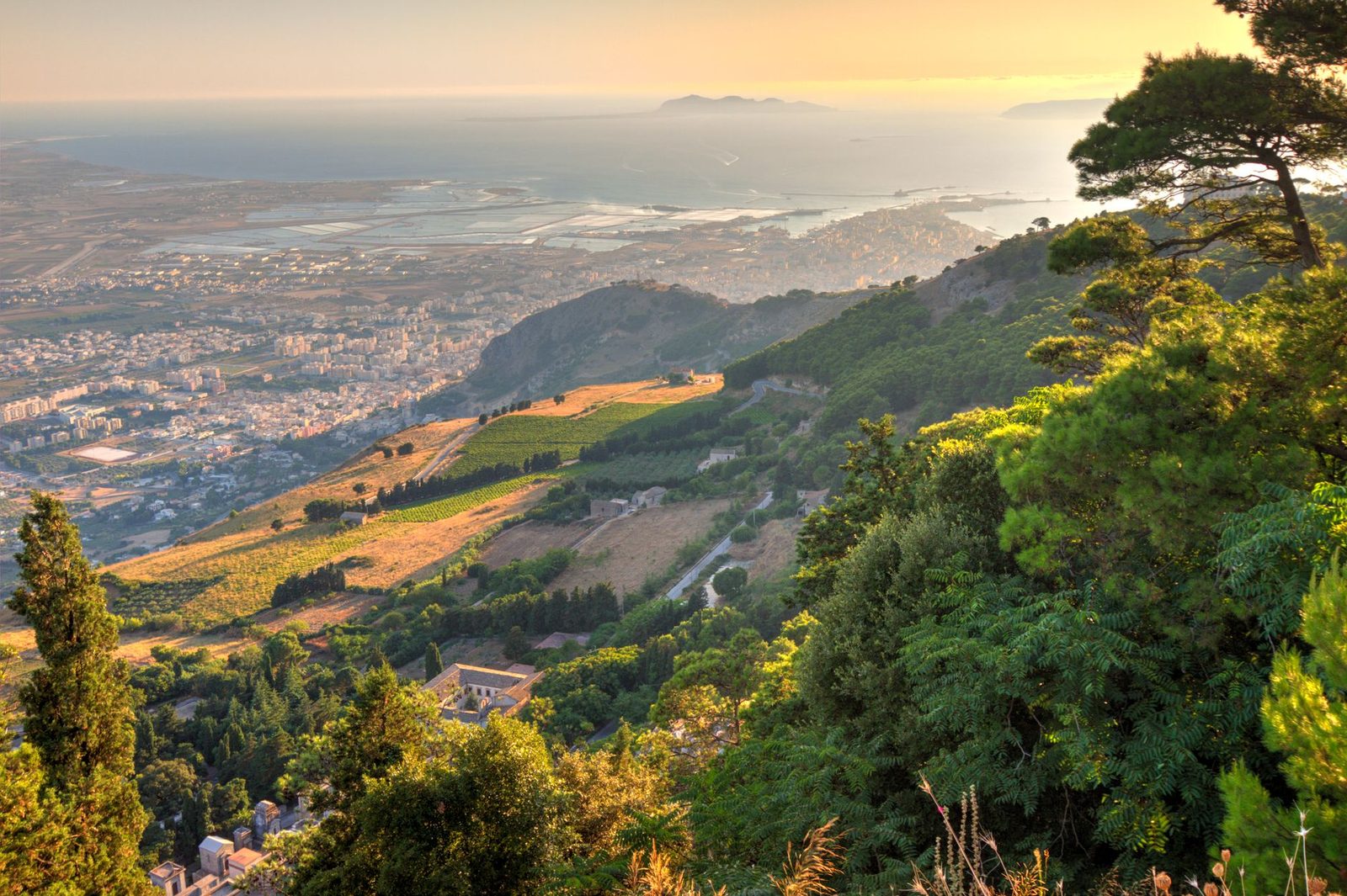 Stunning view of Erice, Sicilia, with lush greenery and the shimmering Mediterranean Sea at sunset.