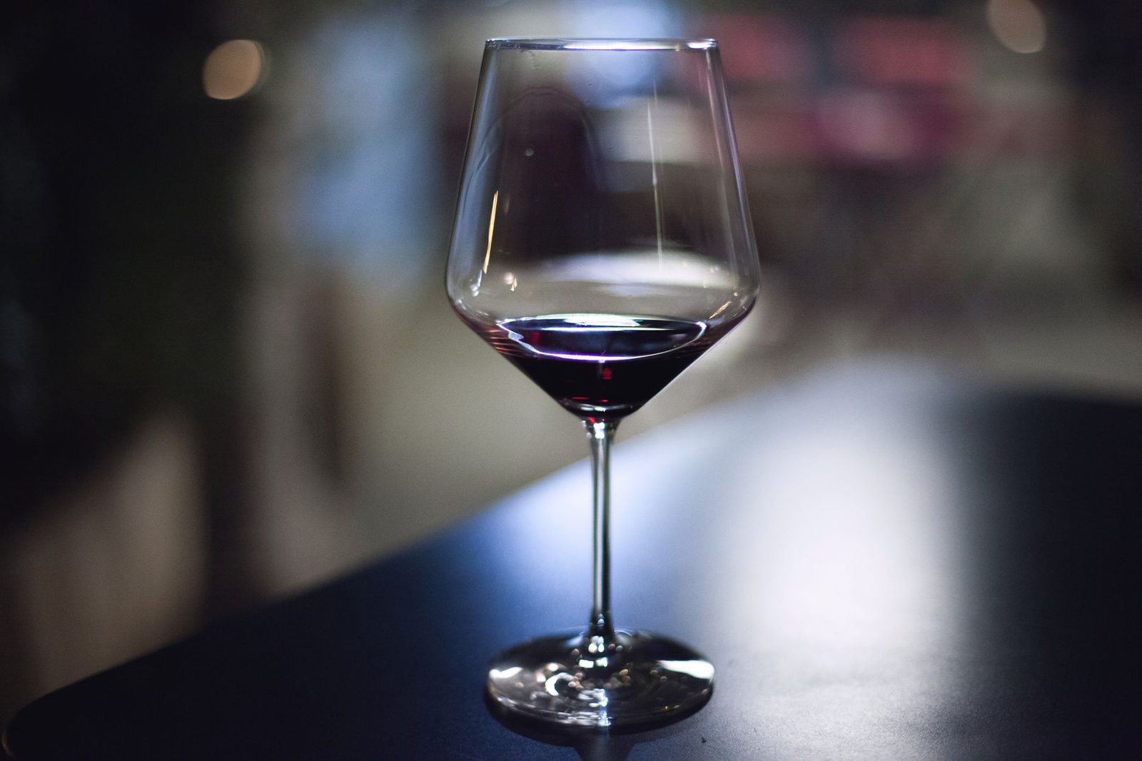 A close-up of a wine glass filled with red wine on a dark table in an indoor setting.