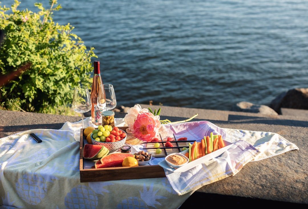 a tray of fruit and a glass of wine on a table by the water
