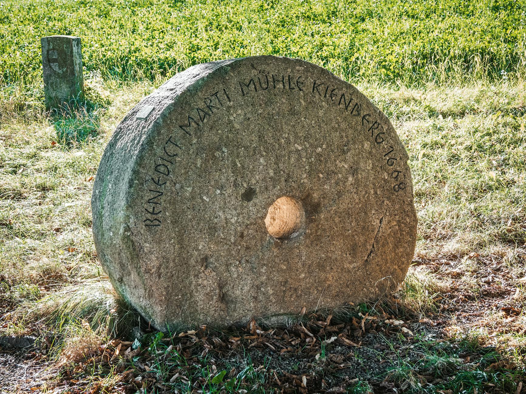 An ancient millstone with inscription rests in a tranquil countryside field.
