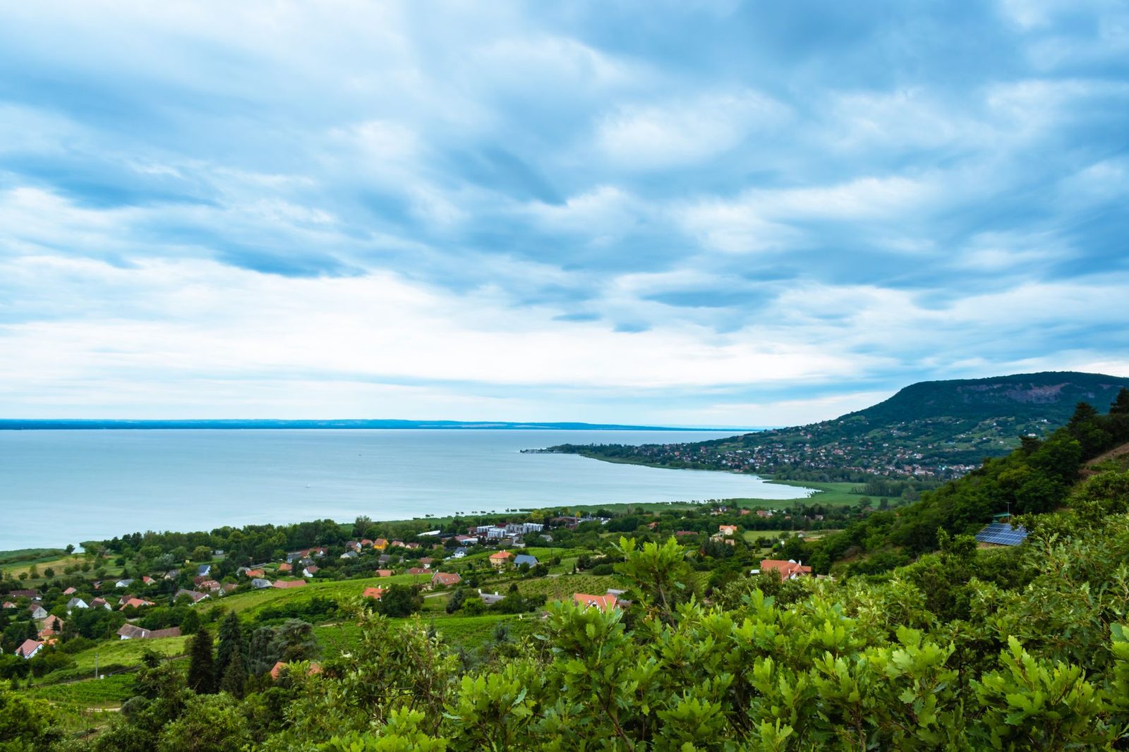 Panoramic view of Badacsonytomaj and Lake Balaton under a cloudy sky in Hungary.