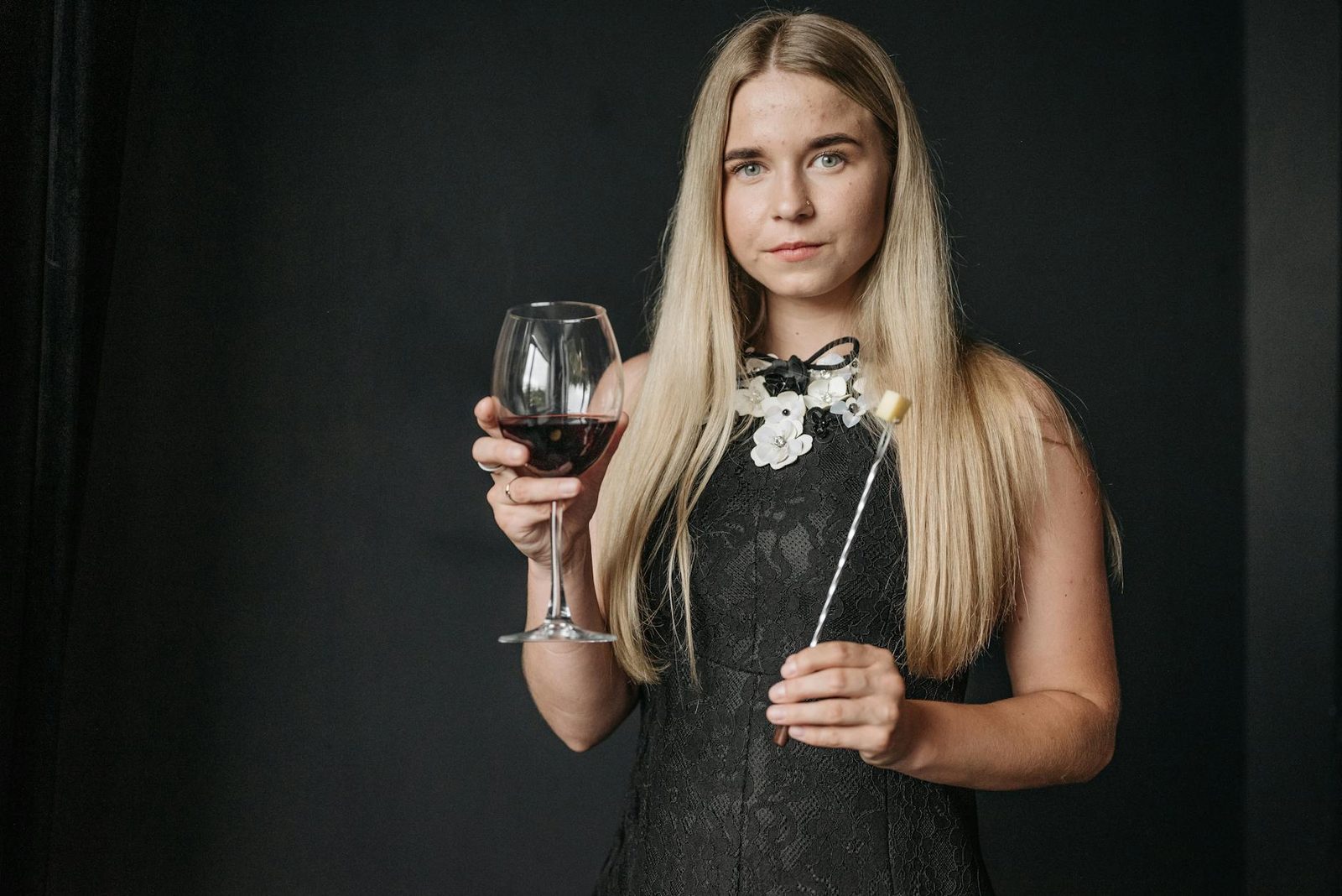 Elegant woman in a black dress holding a glass of red wine against a black background indoors.