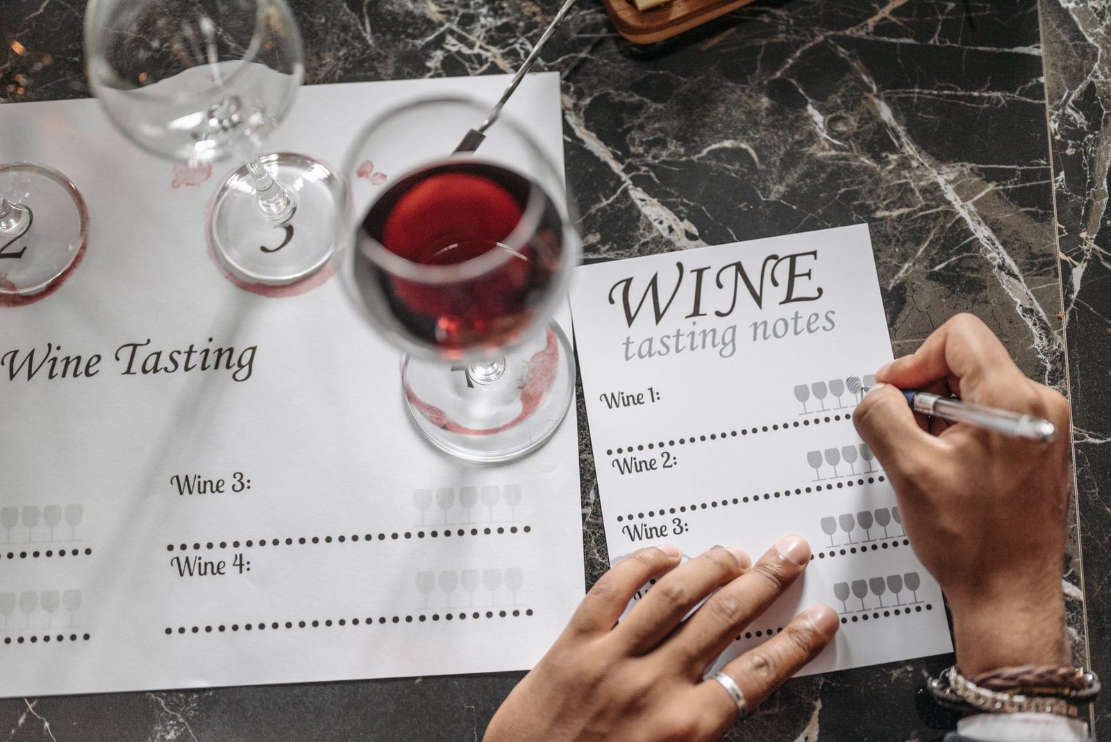 Close-up of wine tasting session with notes, glasses, and marble surface.
