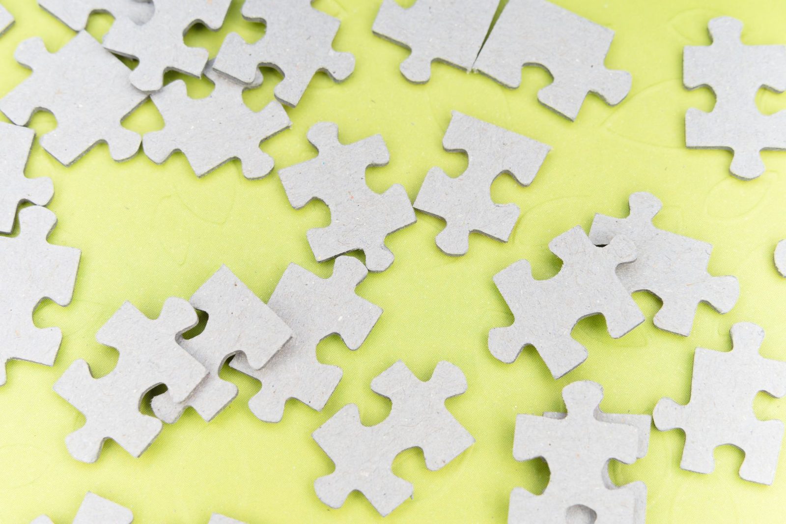 Close-up of gray puzzle pieces scattered on a vibrant yellow background for a playful abstract composition.